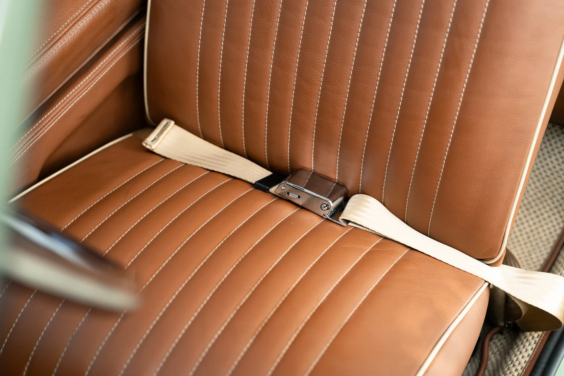 Hand-stitched tan leather bench seat with cream piping and seatbelt